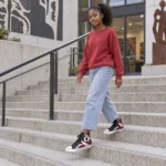 Teen girl wearing black SPEAK//UP high-top sneakers with red and white artwork and loose jeans on concrete city steps.