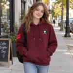 Teenage girl wearing a burgundy SPEAK//UP pullover hoodie with an arrow chest patch and red sleeve stripes on a city sidewalk