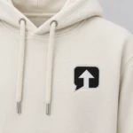Close-up of the black speech-bubble patch with a white arrow and white stitched border on a milk ivory SPEAK//UP hoodie
