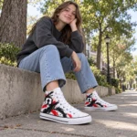 Teen girl wearing white SPEAK//UP high-top sneakers with red and black artwork and loose jeans on a tree-lined walkway.